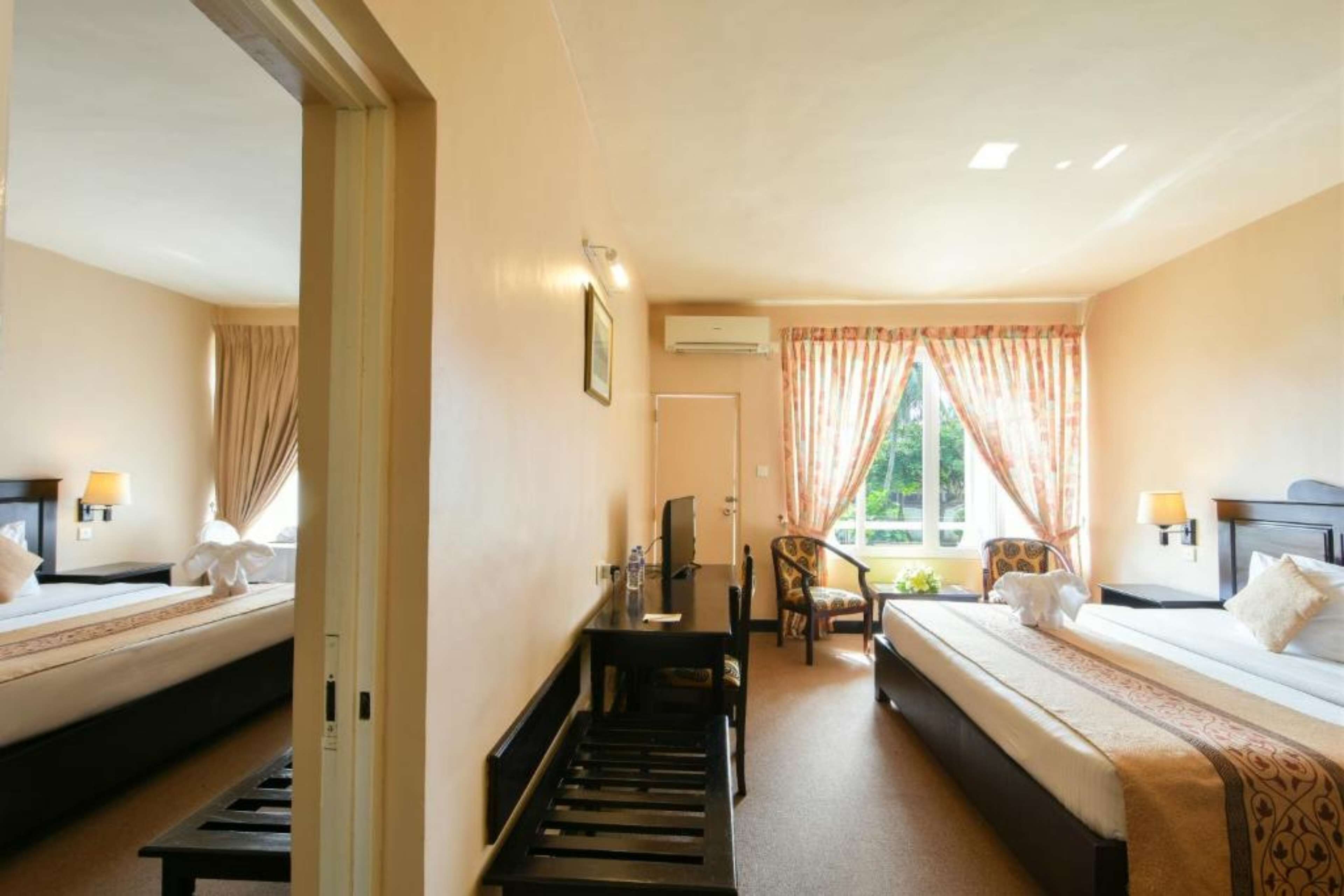 A hotel room with two beds, a desk, a chair, and a window with curtains.