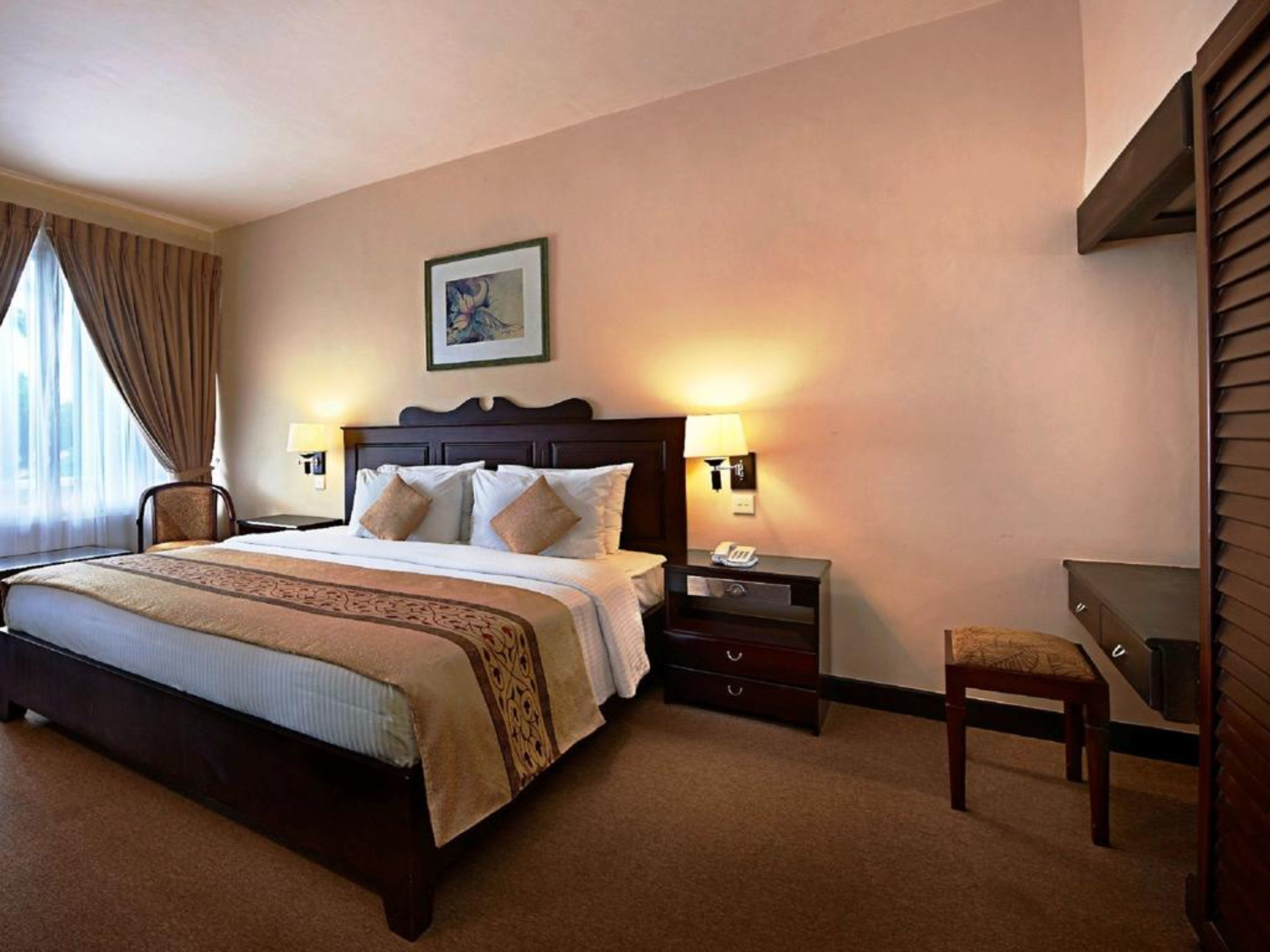 A hotel room with a large bed, two bedside tables with lamps, a chair, and a desk.