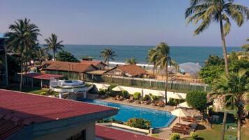 Relax by the resort's pool surrounded by lush greenery and palm trees, with the ocean visible in the background.