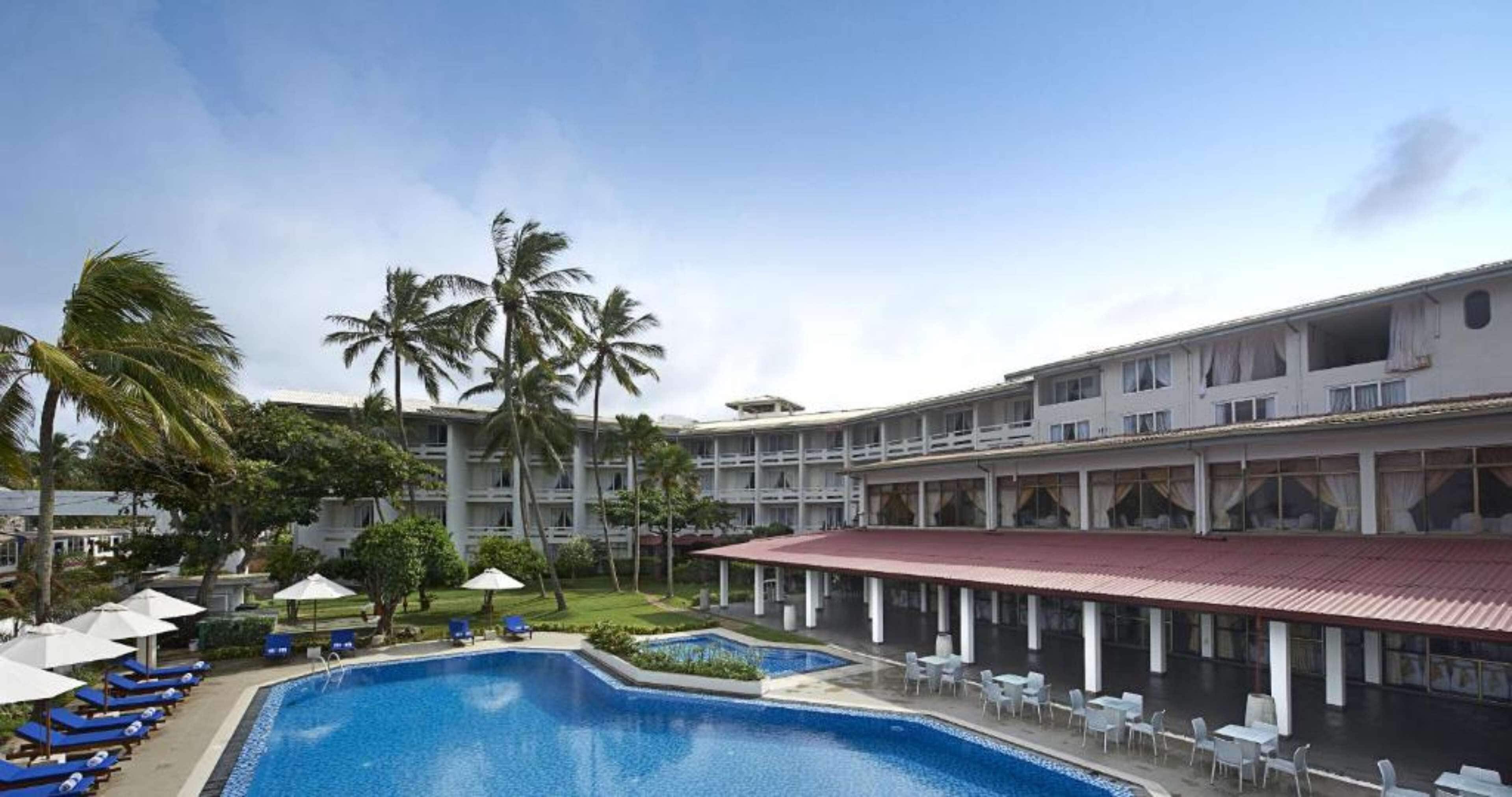 A hotel with a swimming pool, lounge chairs, and palm trees.