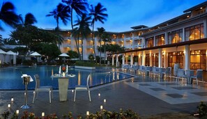 A hotel with a swimming pool, outdoor seating, and palm trees. - Berjaya Hotel Colombo (Mount Lavinia)