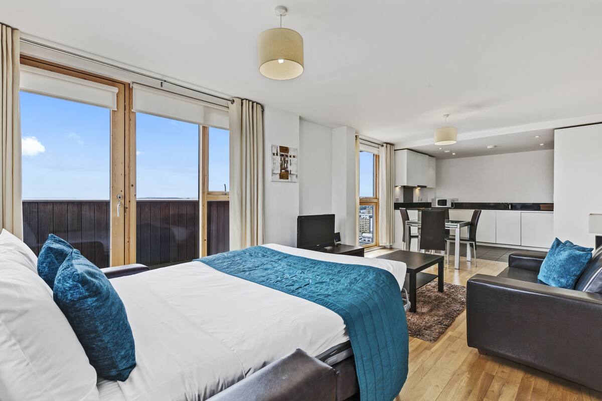 Quarto de hotel moderno com uma cama grande, uma escrivaninha, um sofá e vista para o céu.