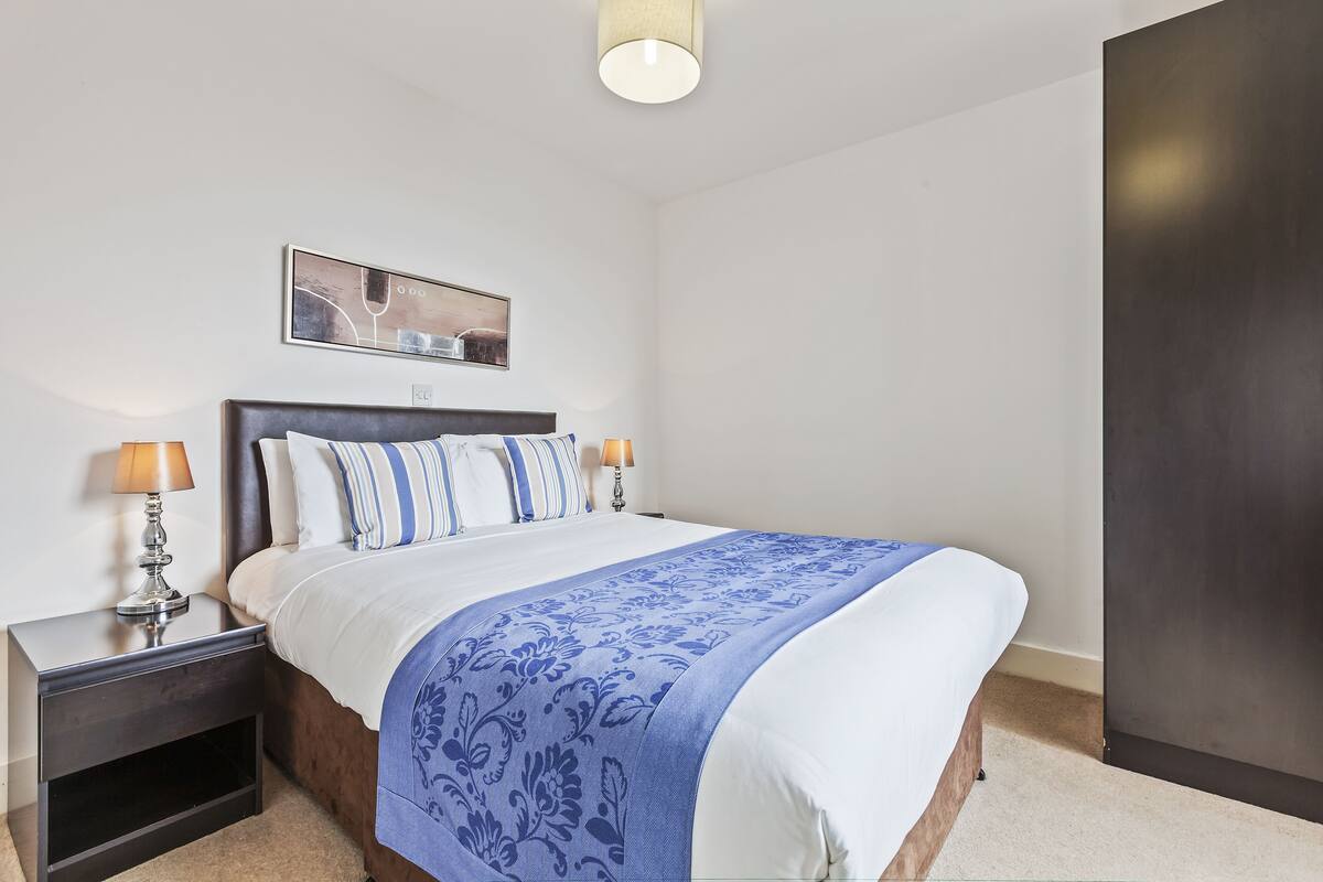 Quarto bem organizado com cama, mesas de cabeceira, abajur e um quadro na parede.