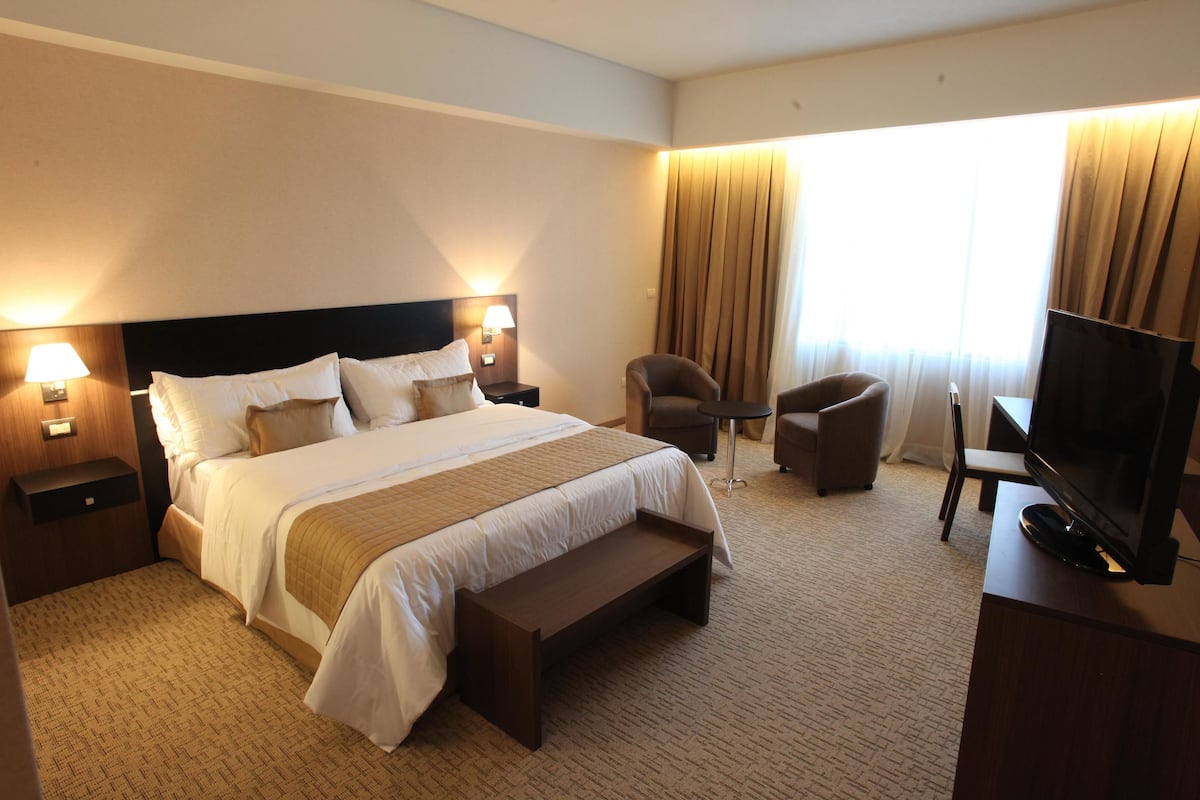 A hotel room with a large bed, bedside tables with lamps, a TV, a desk, and a chair.