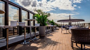 A rooftop terrace with outdoor seating, large windows, and potted plants.