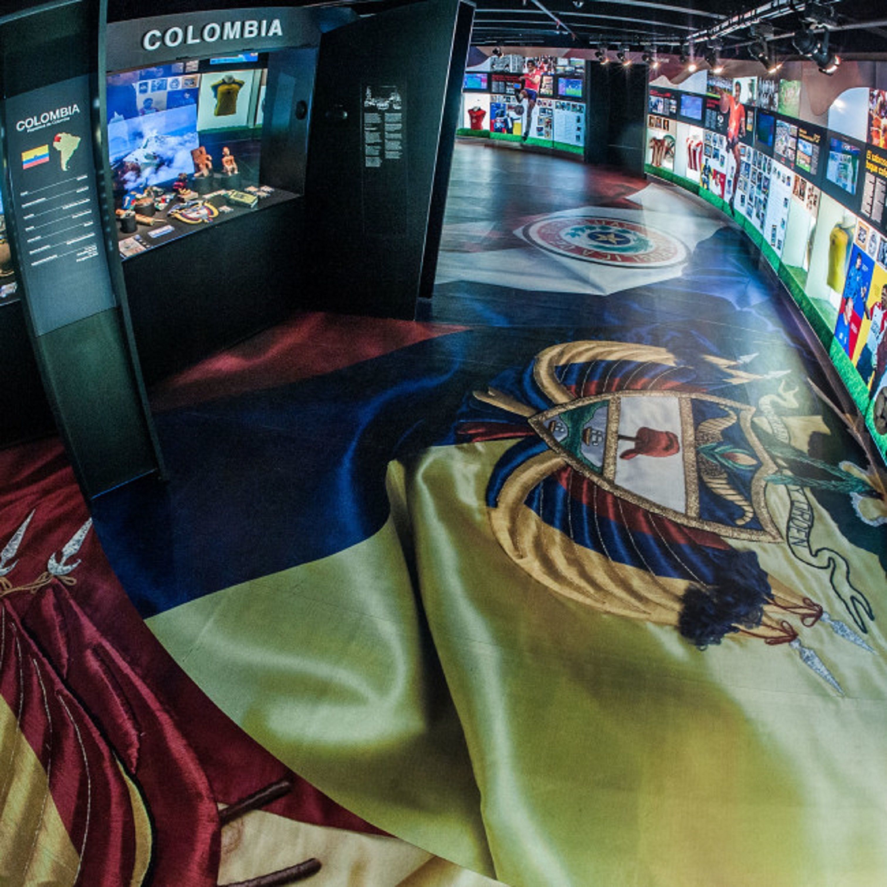 A museum exhibit with a large, colorful map of Colombia, a display case with various items, and a wall with informational posters.