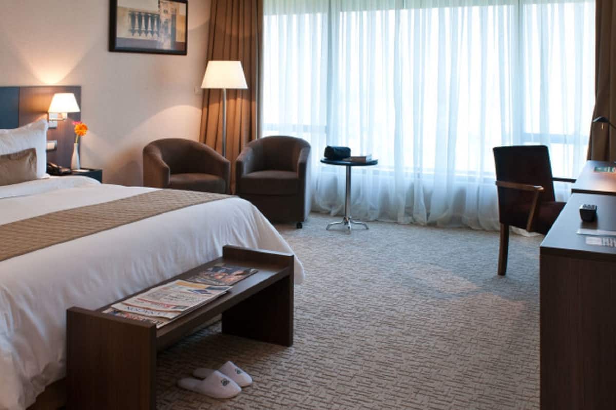 A hotel room with a large bed, two armchairs, a desk, and a small table.