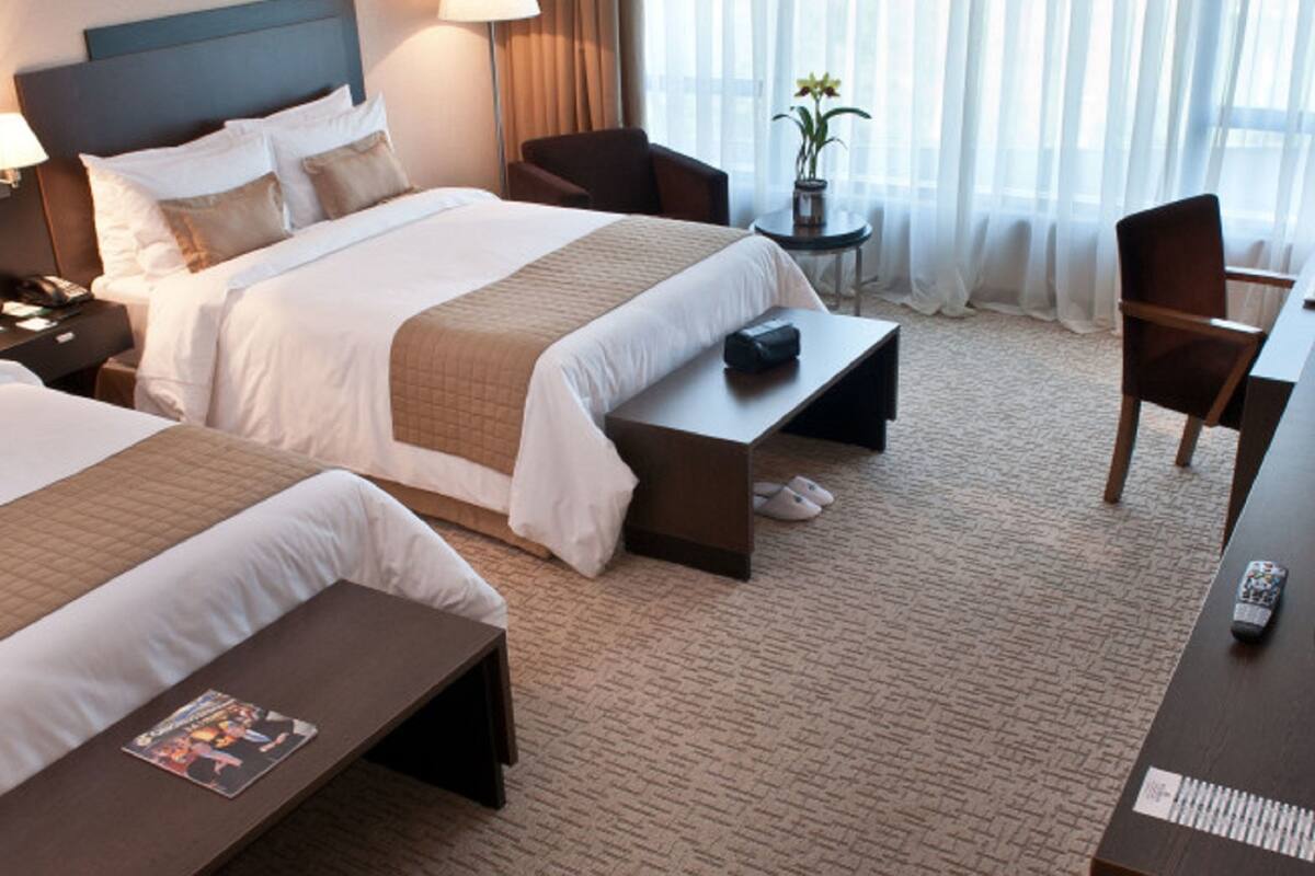 A hotel room with two beds, a desk, a chair, a lamp, and a potted plant.