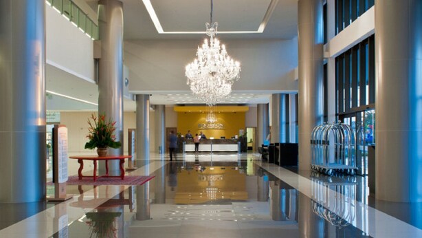A modern hotel lobby with a reflective floor, a central chandelier, and a reception desk.