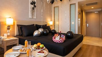 A hotel room with a neatly made bed, a dining table set with breakfast, and balloons.