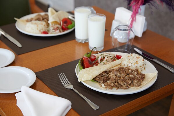 Una mesa de comedor con platos de comida, incluyendo un wrap y arroz, y dos vasos de leche.
