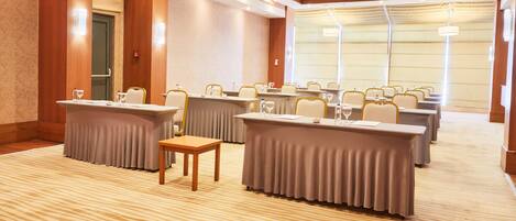 Un salón de conferencias con varias mesas y sillas, piso alfombrado y ventanas amplias.