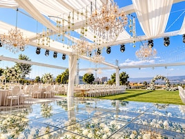 Un espacio para eventos al aire libre con piso de vidrio, mesas blancas y candelabros.
