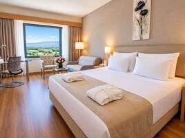 Habitación de hotel con una cama grande, dos sillas, una mesita y vistas al exterior.