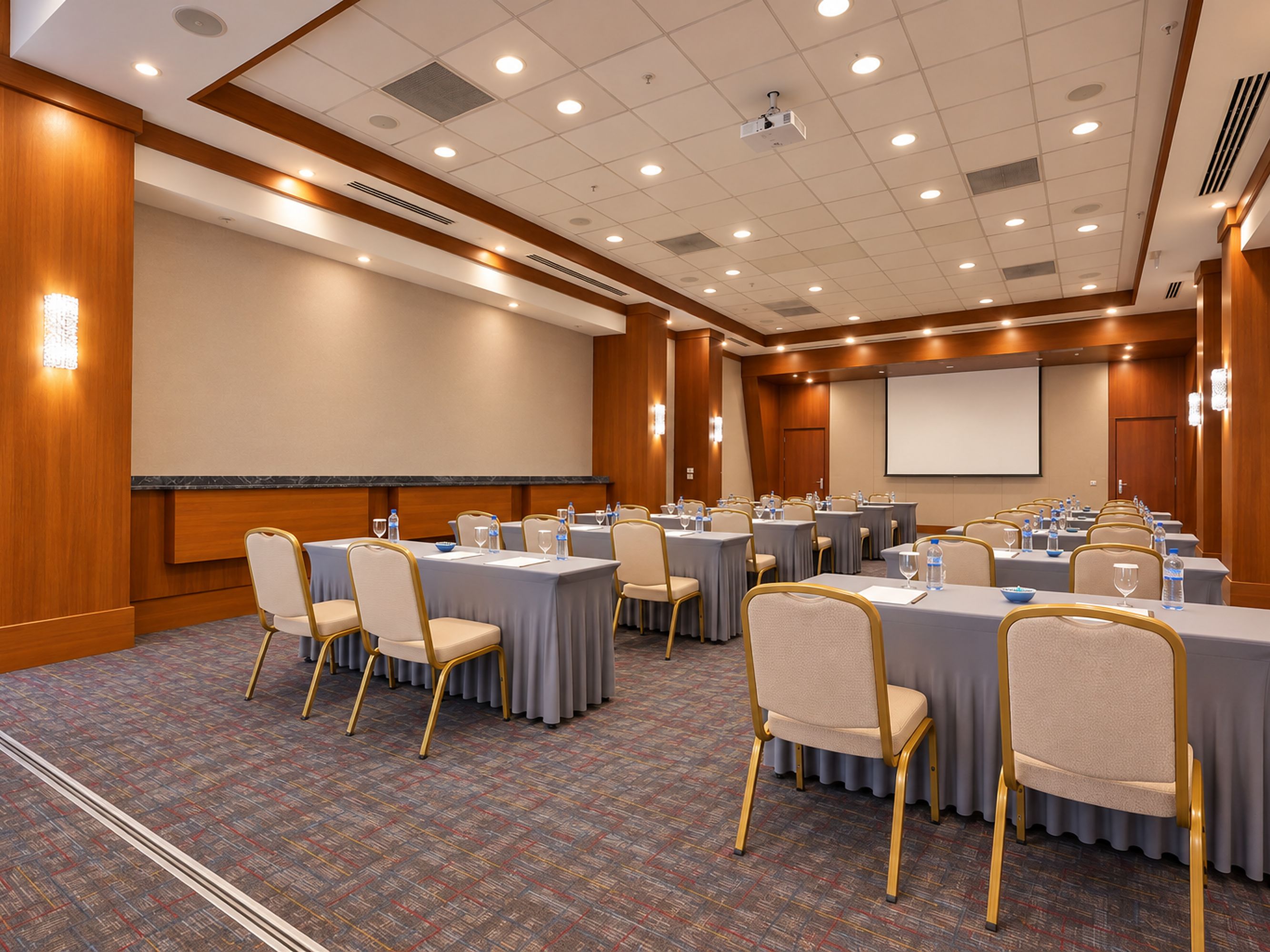 Un salón de conferencias con varias mesas, sillas y una pantalla para proyector.
