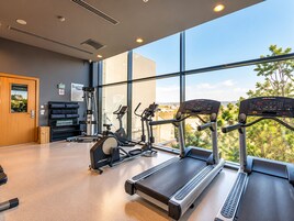 Un gimnasio con cintas de correr, bicicletas estáticas y máquinas de pesas, amplias ventanas y vistas al exterior.