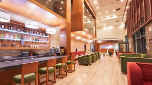 A modern bar area with wooden bar counters, green cushioned bar stools, and a variety of liquor bottles on shelves. - Park Dedeman Denizli (Denizli)