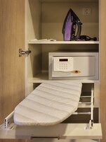 A compact room with a built-in ironing station, a small shelf with a purple iron, and a digital clock.
