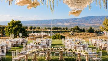 An outdoor wedding venue with round tables, white chairs, and floral arrangements.