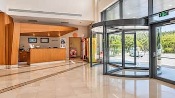A hotel reception area with a wooden reception desk, a reception sign, and a glass door leading outside.