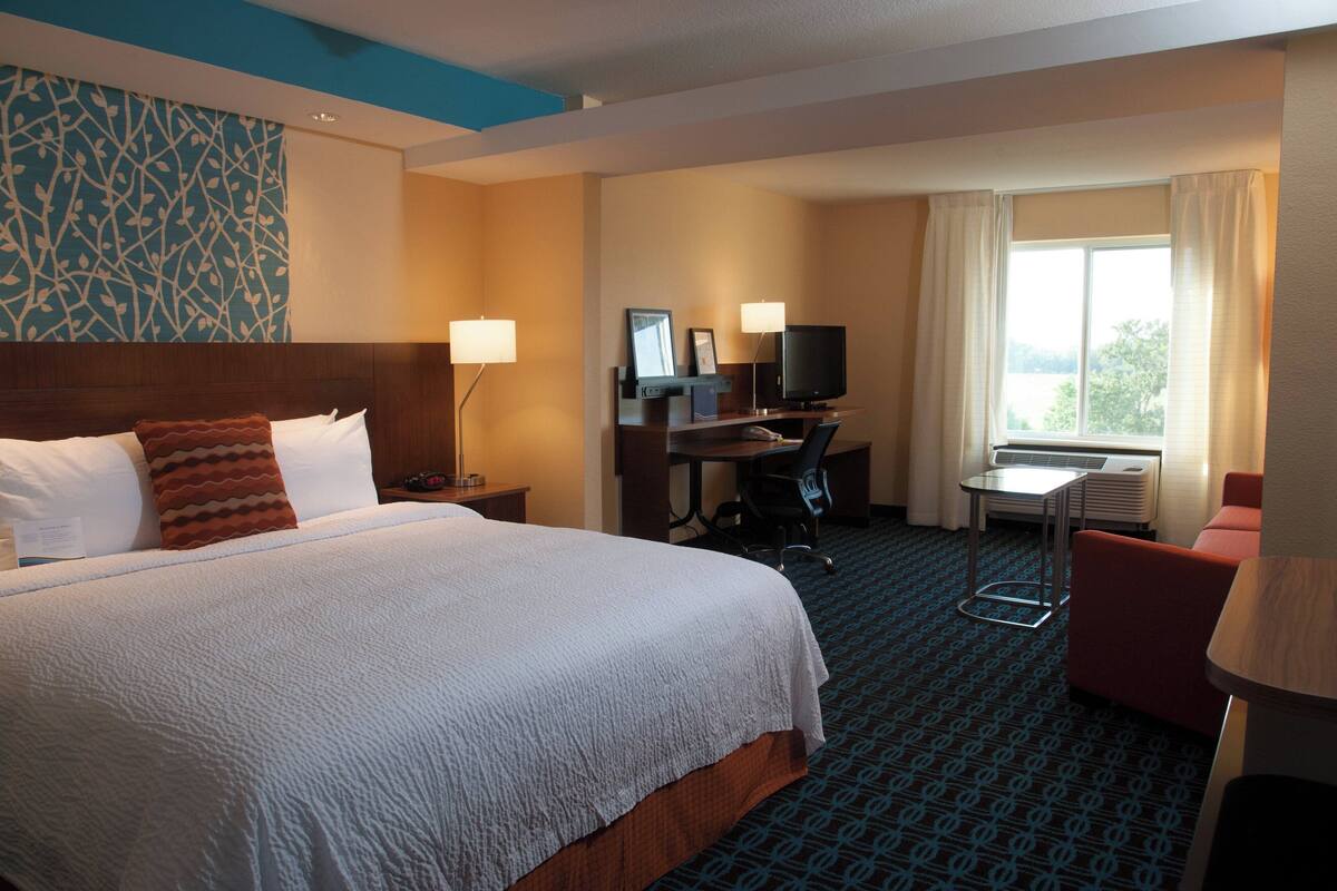 A hotel room with a large bed, a desk with a computer and TV, a small table, and a chair.