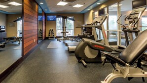 Een fitnessruimte met trainingsapparatuur, een loopband en een hometrainer.