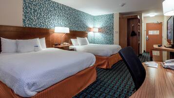 Une chambre d’hôtel avec deux lits, un bureau et une chaise. Il y a des lampes sur le bureau et un miroir au mur.