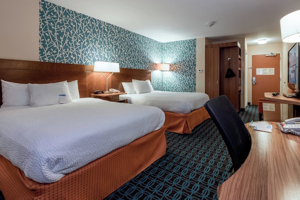 A hotel room with two beds, a desk, and a chair. There are lamps on the desk and a mirror on the wall.