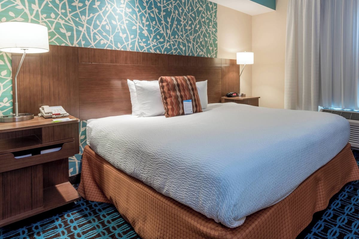 A hotel room with a large bed, wooden headboard, patterned wall, bedside tables with lamps, and a telephone.