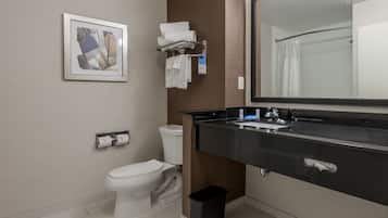 Un baño moderno con inodoro, lavamanos y espejo. Hay un cesto de basura y un perchero con toallas.
