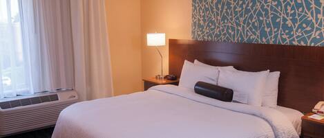 Quarto de hotel com uma cama grande, mesa de cabeceira com abajur, parede com padrão de folhas e janela com cortinas.
