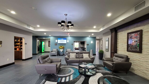 Een ruime lobby met een moderne kroonluchter, comfortabele zithoek, een receptiebalie en een digitaal scherm.