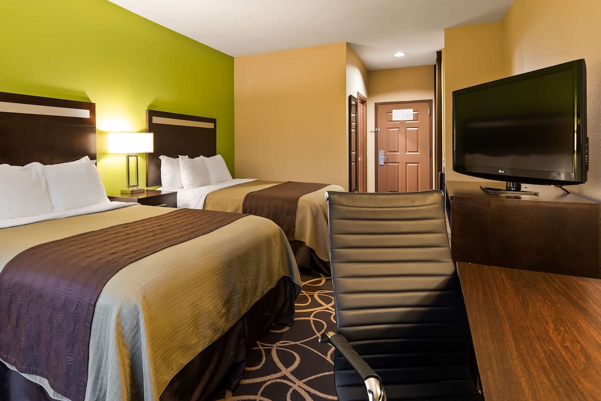 A hotel room with two beds, a desk, a chair, a TV, and a door.