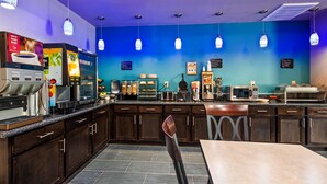 Een moderne koffietent met een blauwe muur, espresso machines, een magnetron en een zitgedeelte.