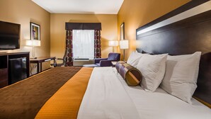 Een hotelkamer met een groot bed, een bureau met een televisie, een stoel en een raam met gordijnen.