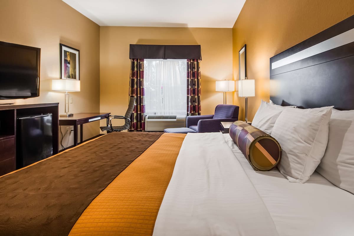 A hotel room with a large bed, a desk with a television, a chair, and a window with curtains.