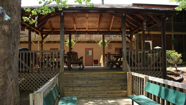 A wooden covered porch with benches, a staircase, and a building in the background.