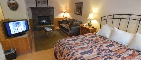 A cozy hotel room with a bed, a television, a fireplace, and a sofa.