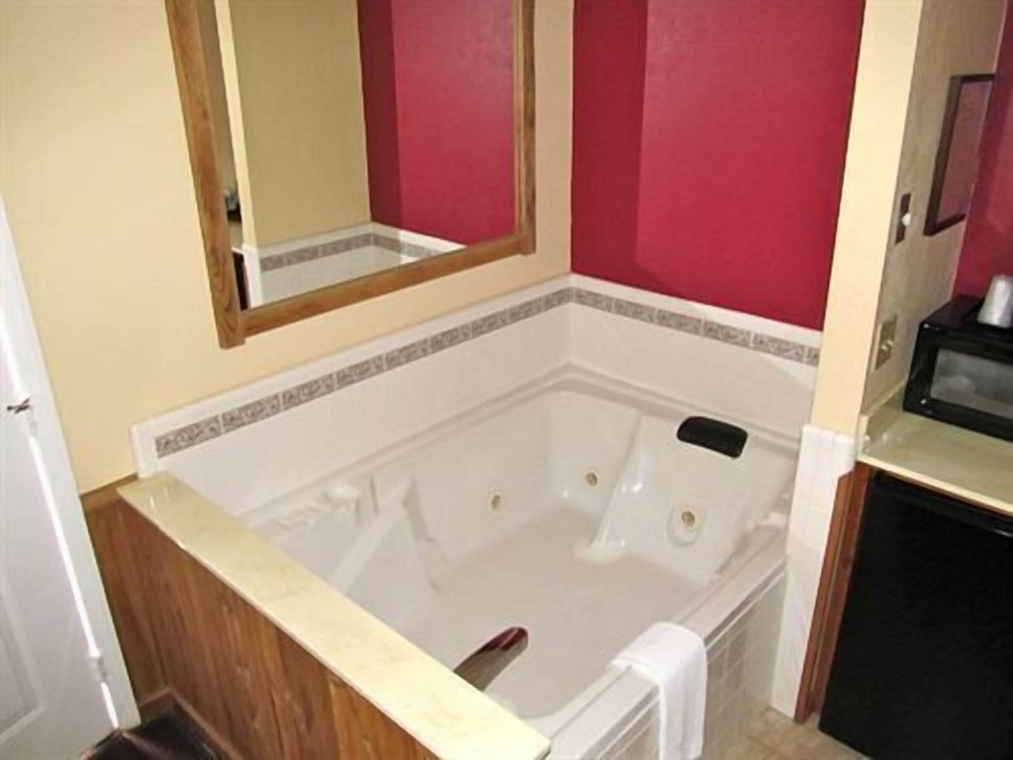 Un baño con una bañera blanca, un tocador de madera, un espejo y un microondas.