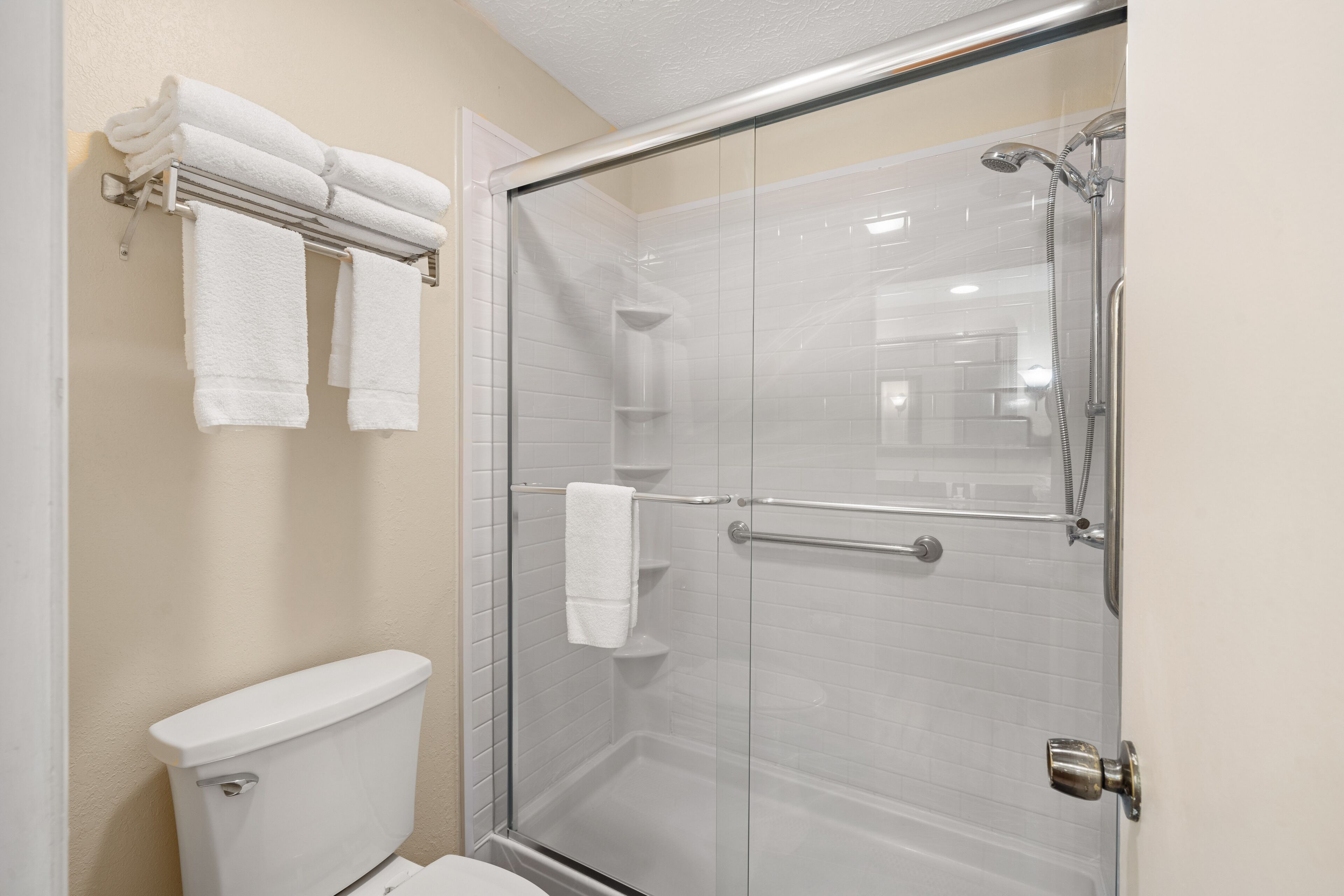 A bathroom with a glass-enclosed shower, a toilet, and a towel rack with folded towels.