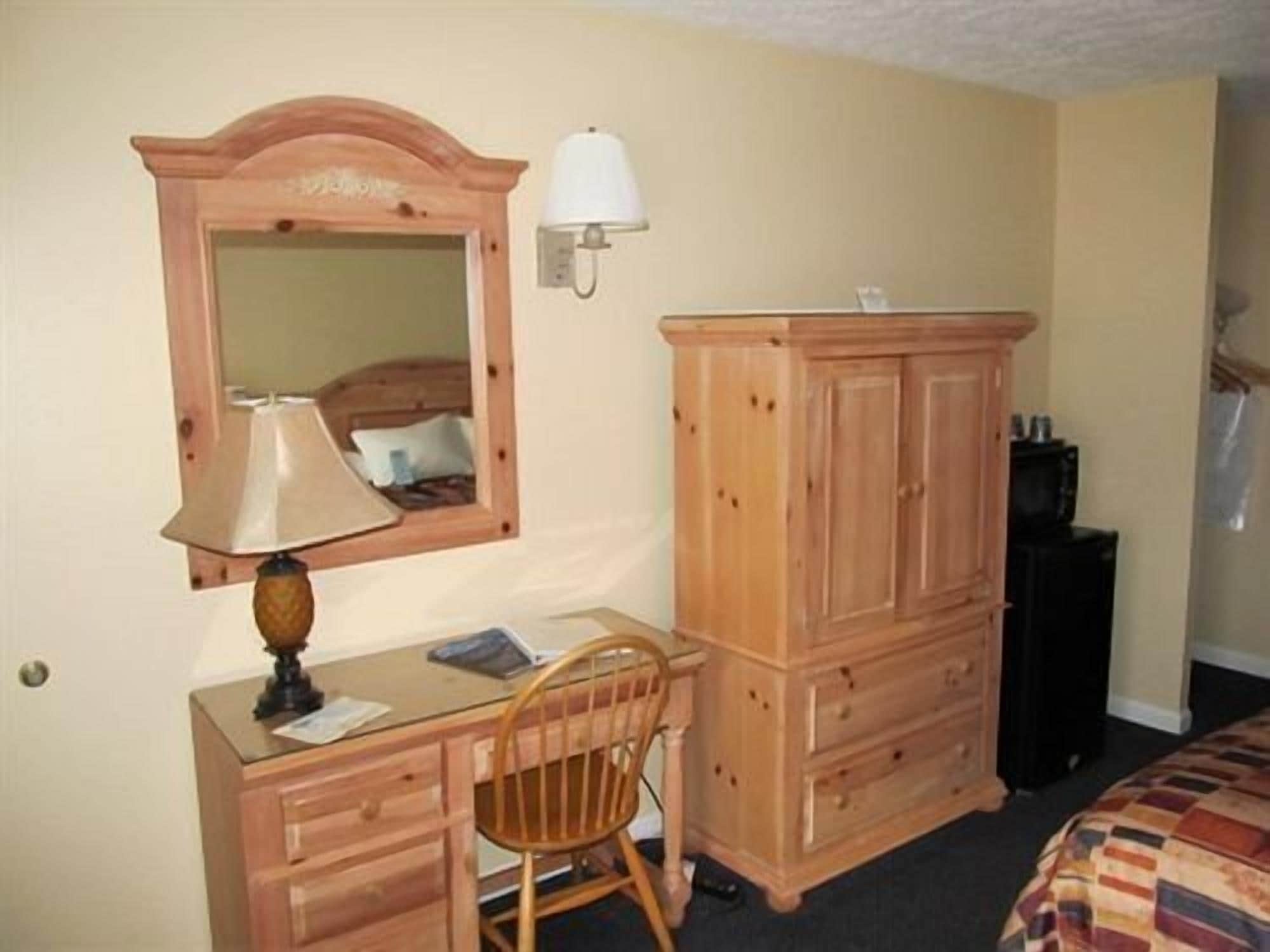 A room with a wooden desk, a chair, a wardrobe, a mirror, and a lamp.