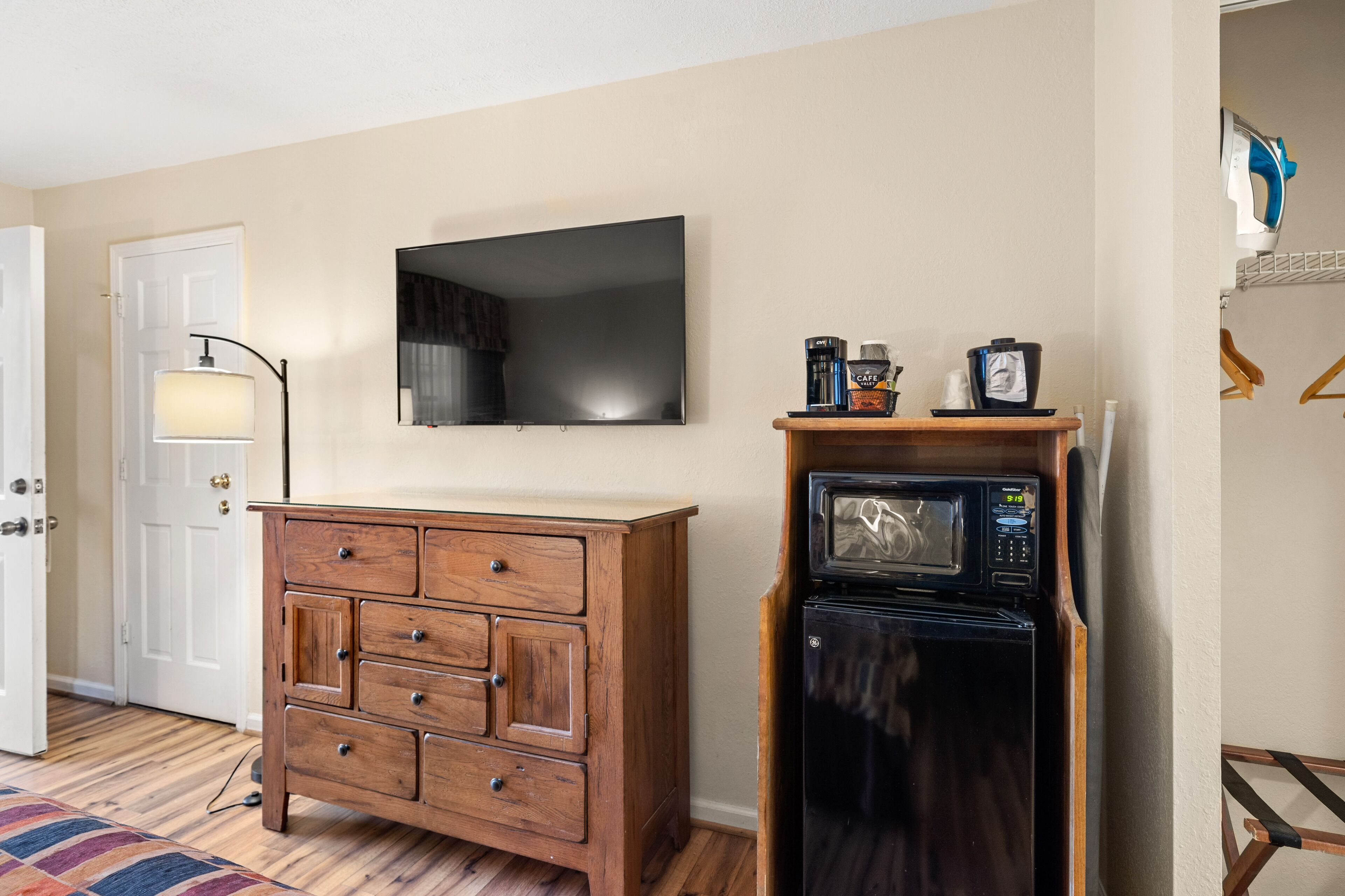 A room with a wooden dresser, a flat-screen TV, a microwave, and a door with a lamp.