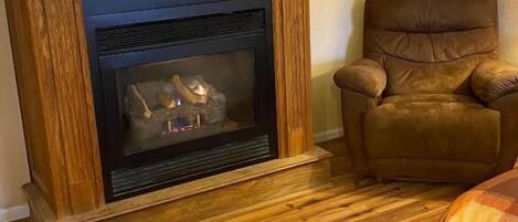 Una sala de estar con chimenea, un sillón de cuero marrón y piso de madera.