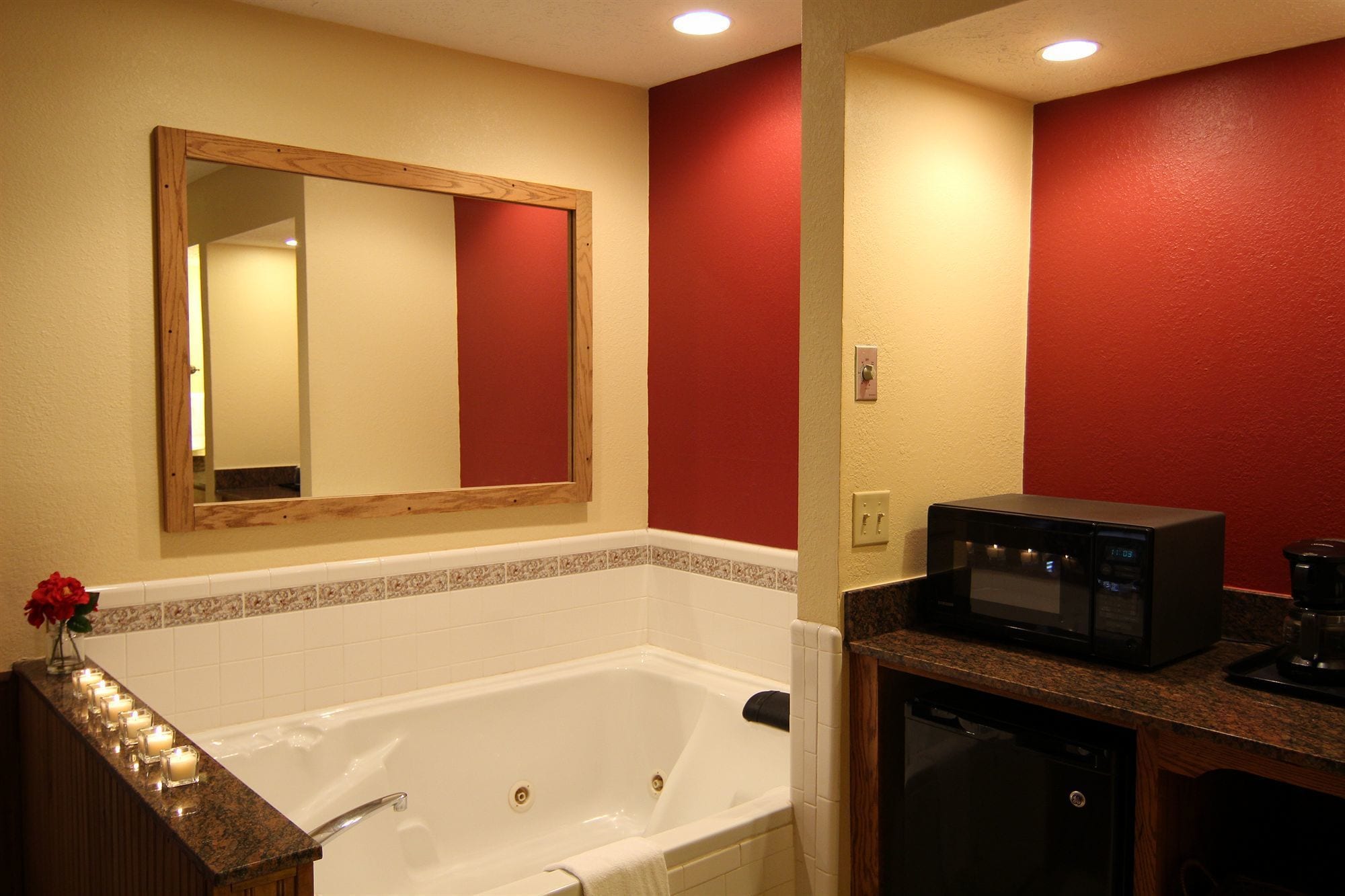 A bathroom with a bathtub, a mirror, a microwave, and a sink.