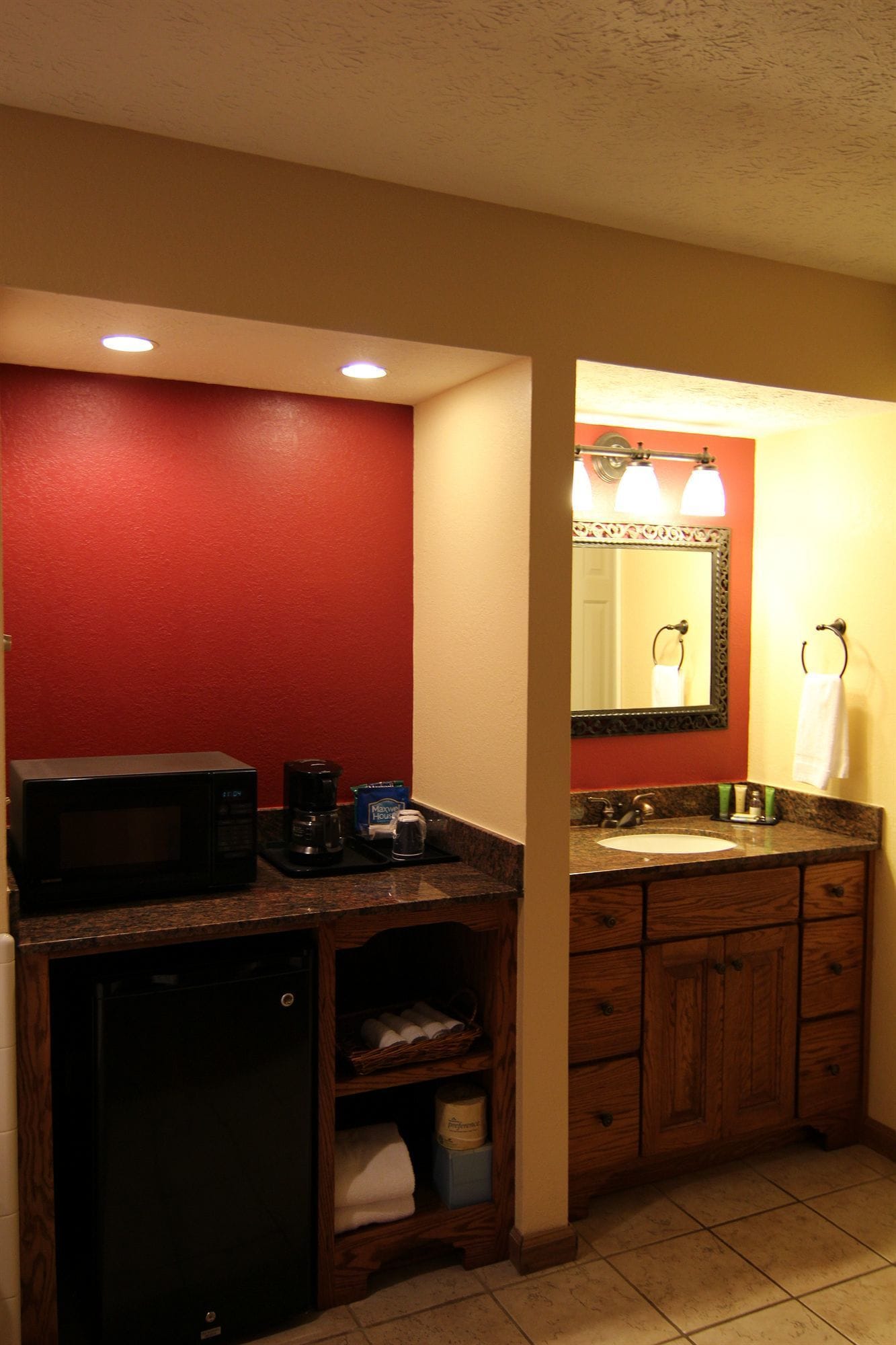 Ein kleines Badezimmer mit roter Wand, Waschbecken mit Spiegel, Mikrowelle und kleines Schränkchen.