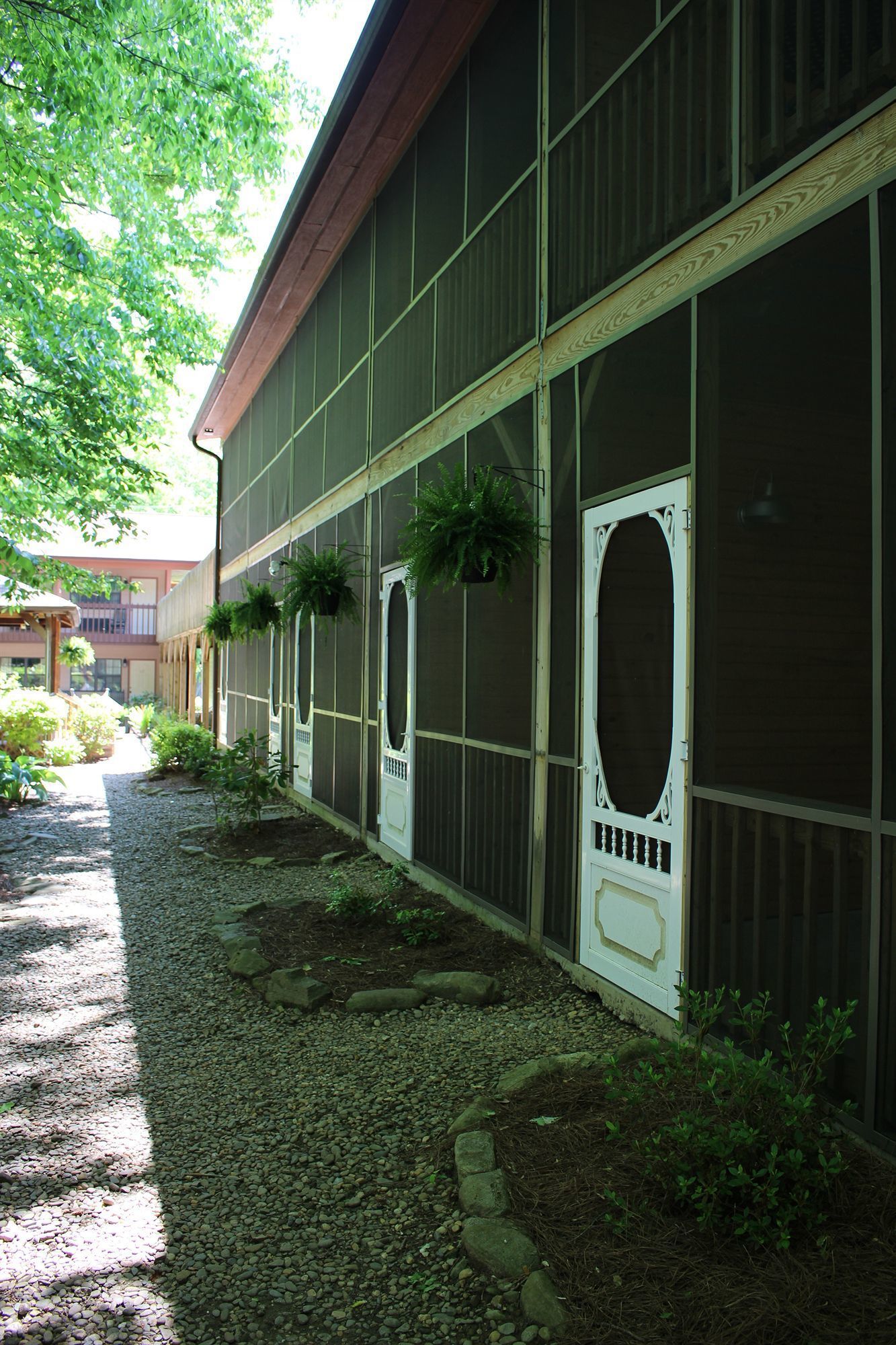 Un edificio con varios ventanales y puertas, algunas decoradas. Hay plantas colgando de las ventanas y un camino de grava que lleva a la entrada.
