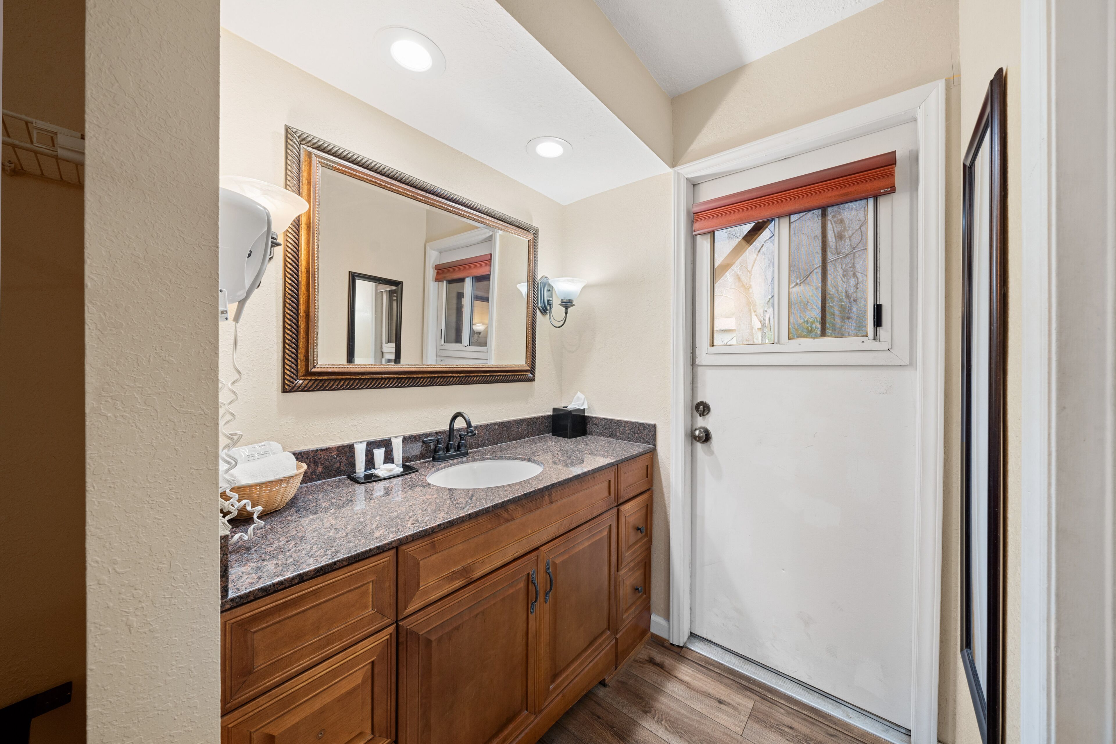 A bathroom with a double sink vanity, wooden cabinets, a large mirror, and a door with a window.