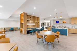Un comedor moderno con mesas y sillas, una zona de cocina con encimera azul y un separador de madera con estantes.
