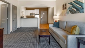 A modern living room with a grey sofa, a coffee table, and a kitchen in the background. - Comfort Inn & Suites Verona at Turning Stone Resort Casino (Verona)