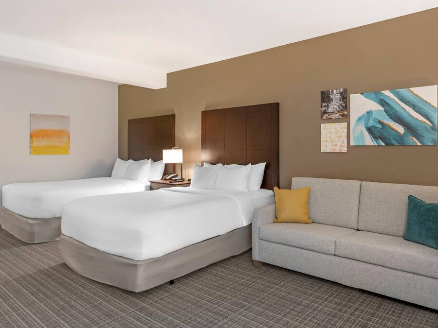 Habitación de hotel con dos camas, un sofá, una lámpara y obras de arte en las paredes.